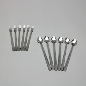 May include: A set of stainless steel forks and spoons. The forks have three tines, and the spoons have round bowls. The utensils are arranged on a light gray surface.