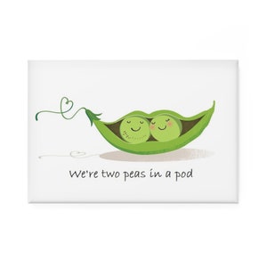 Puede incluir: Una tarjeta blanca con una vaina de guisante verde que contiene dos guisantes. Los guisantes tienen caras sonrientes y mejillas rosadas. El texto "We're two peas in a pod" está escrito debajo de la vaina.