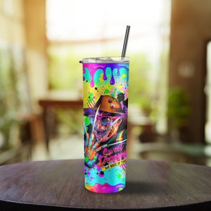 May include: A colorful stainless steel tumbler with a graphic of Freddy Krueger from the movie "A Nightmare on Elm Street". The tumbler has a black lid and a black straw. The graphic is surrounded by colorful paint splatters and the text "Sweet Dreams Are Made Of This".