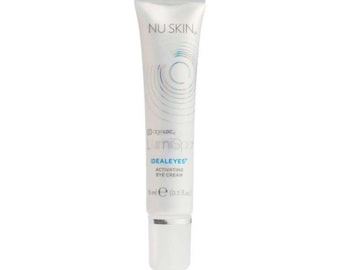 May include: A white tube of Nu Skin IdealeEyes Activating Eye Cream. The tube has a silver cap and features the Nu Skin logo and product information in blue and black. The tube contains 15 ml (0.5 fl oz) of eye cream.