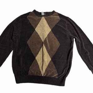 May include: A long-sleeved crew neck sweater in a dark brown shade featuring a prominent argyle pattern on the front. The pattern consists of large, vertically aligned diamonds in alternating shades of light tan and medium brown.