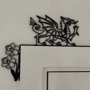 May include: Black metal wall decor featuring a Welsh dragon and daffodils. The dragon is facing right and has its wings spread. The daffodils are on the left side of the dragon and have three flowers.