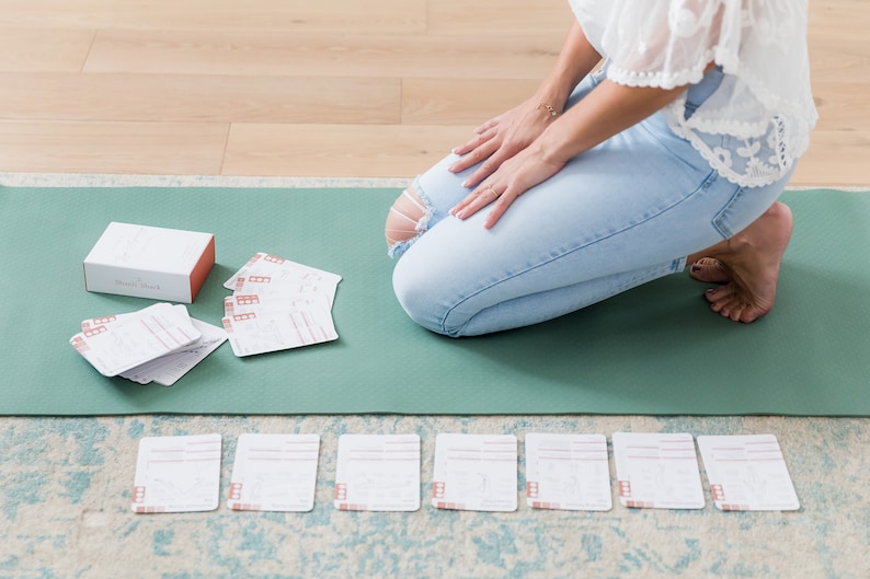 A green yoga mat with a white box labelled "Soul Seek" and a stack of white cards with red accents. There are also seven white cards with red accents laid out in a row on a light brown surface.