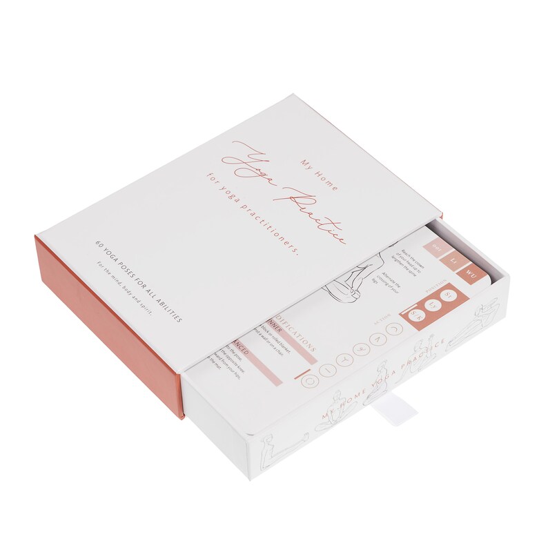 A white box with a pink lid, open to reveal a deck of cards with illustrations of yoga poses. The box has the text "My Home Yoga Practice for yoga practitioners." and the cards have the text "60 Yoga Poses for All Abilities For the mind, body and spirit."