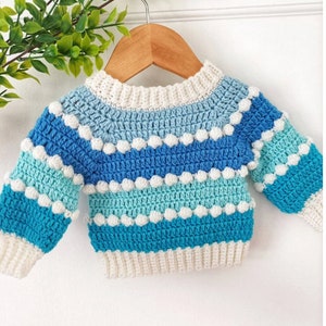 May include: A blue and white striped crocheted baby sweater with white pom-poms.
