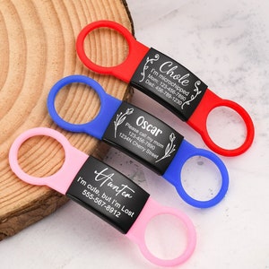 Könnte beinhalten: Drei personalisierte Haustier-ID-Tags mit schwarzem graviertem Text und floralen Designs. Die Tags sind an roten, blauen und rosa Silikon-Schlaufen befestigt. Der Text auf den Tags lautet "Chole", "Oscar" und "Hunter".