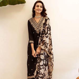 Puede incluir: Una kurta negra bordada con un dupatta de estampado floral. La kurta tiene un escote en V y bordados dorados. El dupatta es transparente y tiene un estampado floral en blanco y negro.