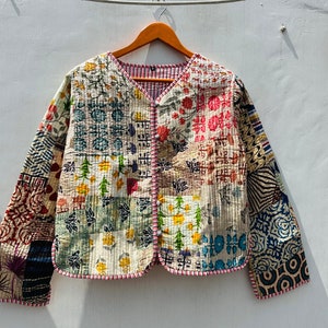 Puede incluir: Una chaqueta acolchada de patchwork con cuello en V y mangas largas. La chaqueta está hecha de una variedad de telas en diferentes colores y patrones, incluyendo flores, geométricos y paisley. La chaqueta tiene un cierre de botón y un ribete rojo y blanco.