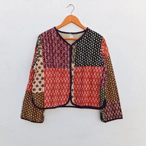 May include: A patchwork quilted jacket with a button closure. The jacket is made of different fabrics with various floral and geometric patterns in shades of red, brown, black, and white.