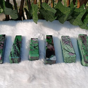 May include: Six green, black, and pink gemstone bars with a smooth, polished finish. The bars are arranged in a row on a white, fluffy surface.