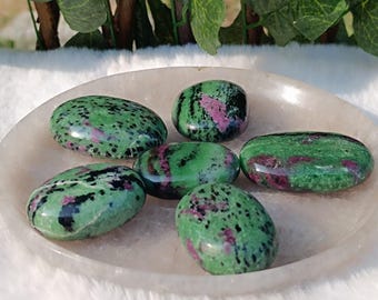 Op de afbeelding: Zes gladde, ovale, groene, roze en zwarte edelstenen, die op een wit bord liggen.
