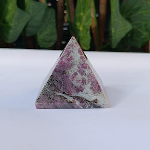 May include: A pink and grey crystal pyramid. The pyramid is made of a polished stone with a swirling pattern of pink and grey.