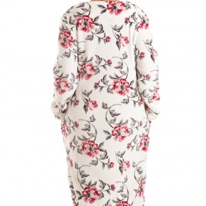 Puede incluir: Una bata larga blanca con estampado floral con flores rosas y grises. La bata tiene mangas largas y cuello en V.