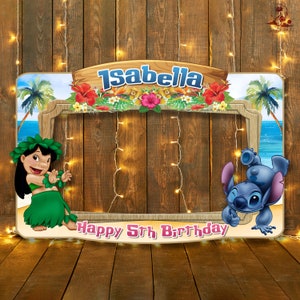 Puede incluir: Un accesorio de cabina de fotos con temática de luau tropical con cielo azul, palmeras y flores. El accesorio tiene un recorte en el medio para la cara de una persona. El texto "Isabella Happy 5th Birthday" está en la parte inferior del accesorio. Los personajes de Lilo y Stitch están a cada lado del recorte.