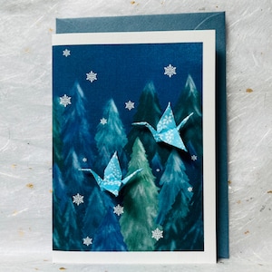 Carte de voeux de Noël faite main - Deux grues en origami au crépuscule au-dessus d'une forêt enneigée