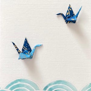 Op de afbeelding: Gelukkige Vaderdag kaart met twee blauwe origami-kranen en een blauw en wit golfpatroon aan de onderkant.