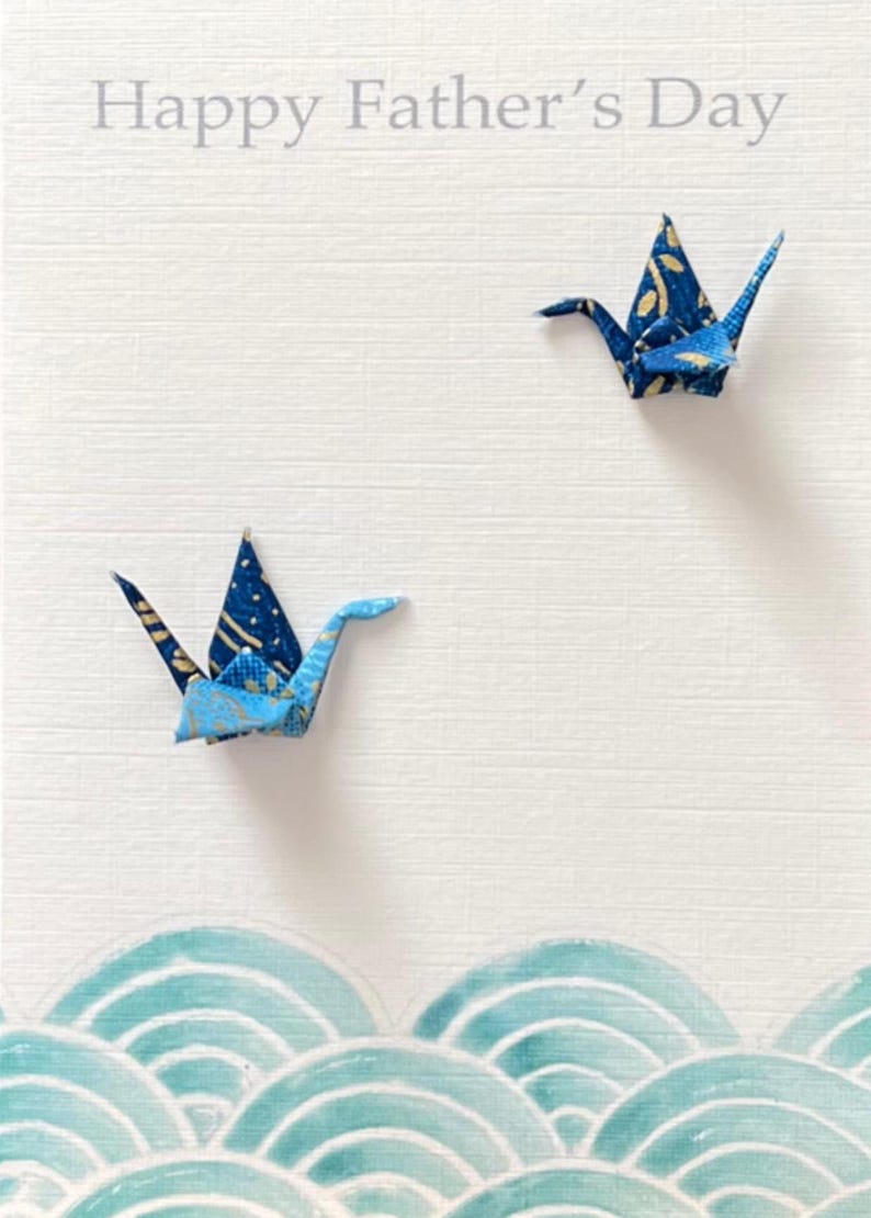 Op de afbeelding: Gelukkige Vaderdag kaart met twee blauwe origami-kranen en een blauw en wit golfpatroon aan de onderkant.