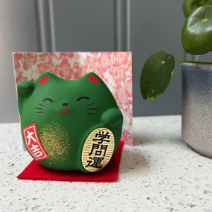 Chat porte-bonheur vert japonais Maneki Neko pour réussir son éducation avec un tapis et une carte d'exposition. Feng-shui.