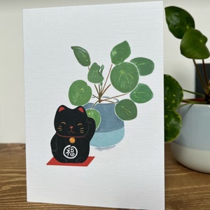 Japanische Grußkarte Niedliche schwarze Glückskatze und Geldpflanze Pilea peperomioides