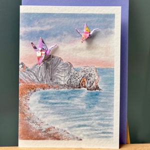 Carte de voeux faite main : deux grues en origami au-dessus de Durdle Door au coucher du soleil