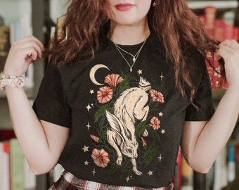 May include: Black t-shirt with a white rabbit, moon, and flowers graphic. The shirt is paired with a red and white plaid skirt.