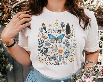 May include: A white t-shirt with a colorful floral and butterfly design. The design features blue, yellow, and green butterflies, as well as various flowers and leaves.
