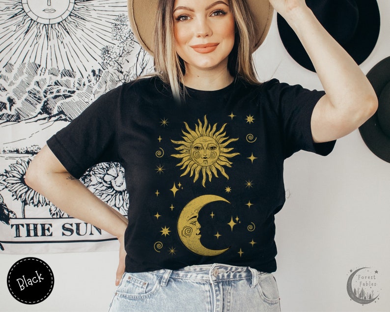 May include: A black t-shirt with a gold sun and moon design. The sun and moon have faces and are surrounded by stars. The text "Forest Fables" is visible in the lower right corner of the image.