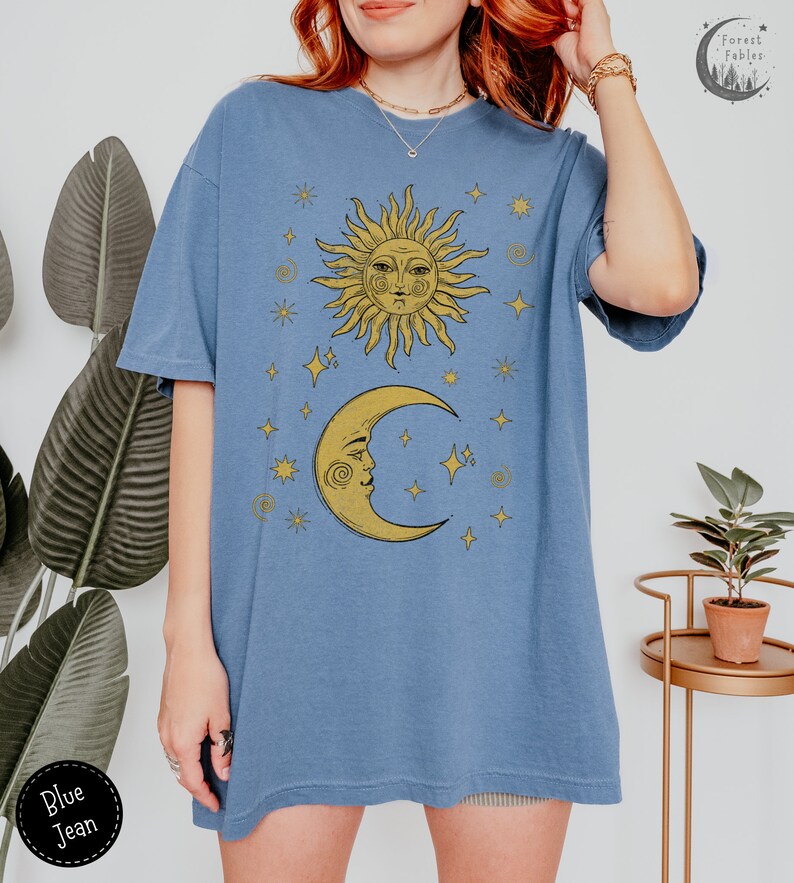 Puede incluir: Una camiseta azul de gran tama&ntilde;o con un gr&aacute;fico amarillo de sol y luna. El sol y la luna tienen caras y est&aacute;n rodeados de estrellas. La camiseta tiene un corte holgado y es perfecta para el uso diario.