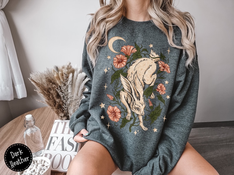 May include: Dark heather grey sweatshirt with a graphic print of a white rabbit with a crescent moon and flowers.