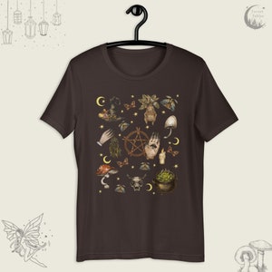 Puede incluir: Una camiseta marr&oacute;n oscuro con un estampado de varios s&iacute;mbolos de brujer&iacute;a, incluyendo un pentagrama, una mano con un ojo, un hongo, un caldero y una calavera. Los s&iacute;mbolos est&aacute;n en tonos de marr&oacute;n, verde y dorado.