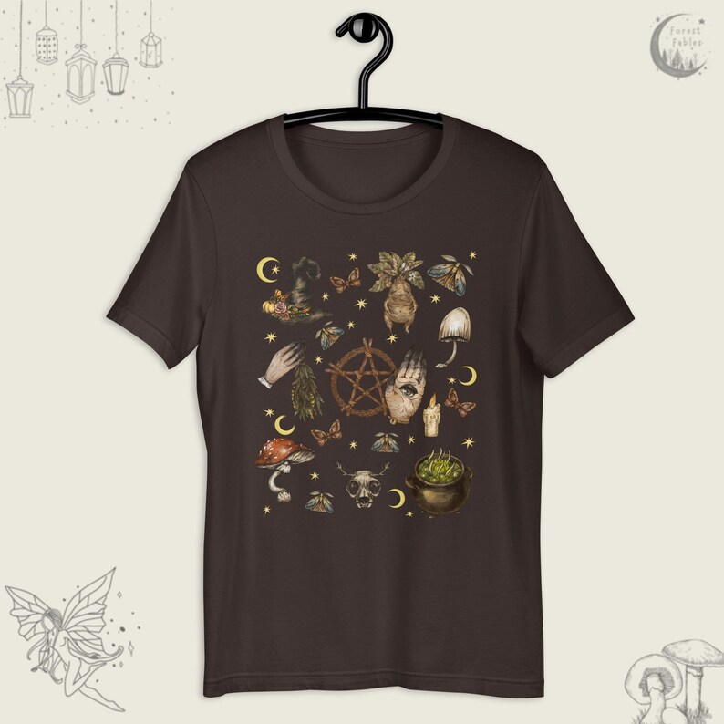 Puede incluir: Una camiseta marr&oacute;n oscuro con un estampado de varios s&iacute;mbolos de brujer&iacute;a, incluyendo un pentagrama, una mano con un ojo, un hongo, un caldero y una calavera. Los s&iacute;mbolos est&aacute;n en tonos de marr&oacute;n, verde y dorado.