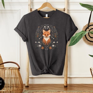 May include: Dark grey heather t-shirt with a graphic of a fox surrounded by flowers. The fox is orange and white with a black nose and eyes.