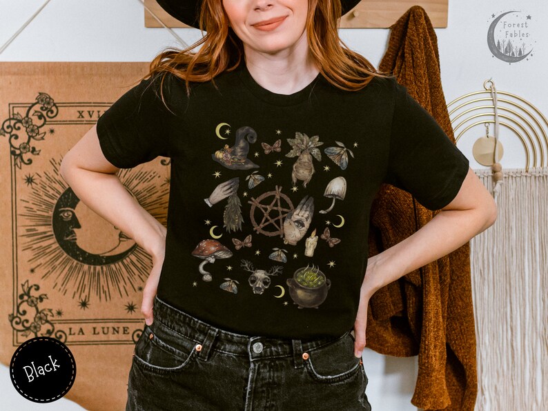 Puede incluir: Camiseta negra con un estampado gr&aacute;fico de un caldero de bruja, setas y otros elementos m&iacute;sticos. El texto "Forest Fables" es visible en la esquina superior derecha de la imagen.