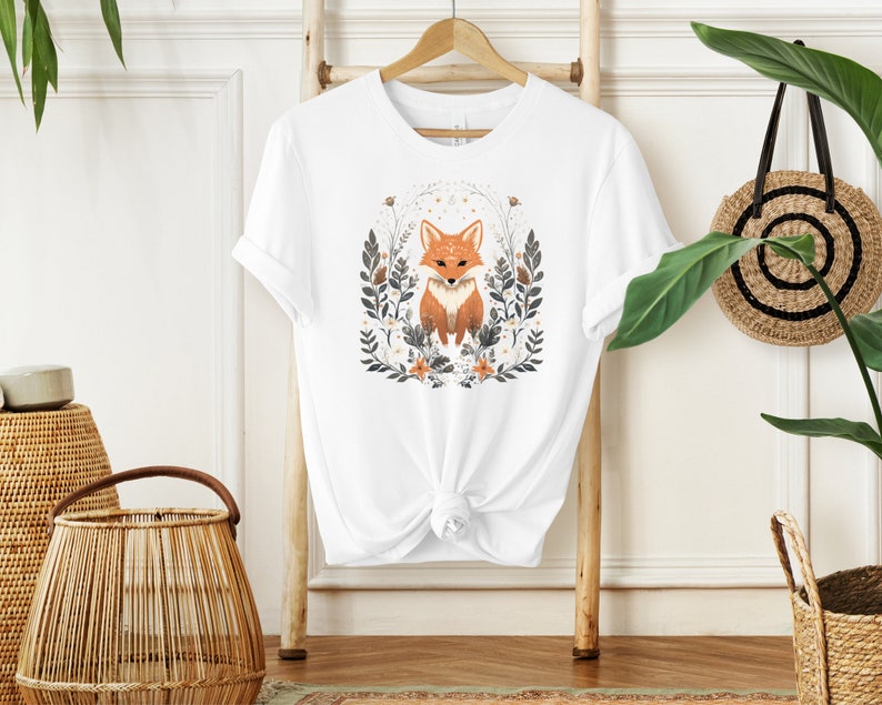 May include: White t-shirt with a graphic of a fox surrounded by flowers and leaves. The fox is orange and white with a black nose and eyes.