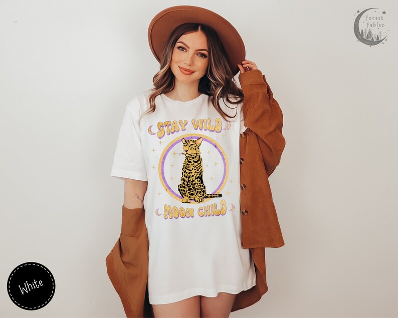May include: White t-shirt with a graphic of a cat sitting with the text "Stay Wild Moon Child" in a retro font.