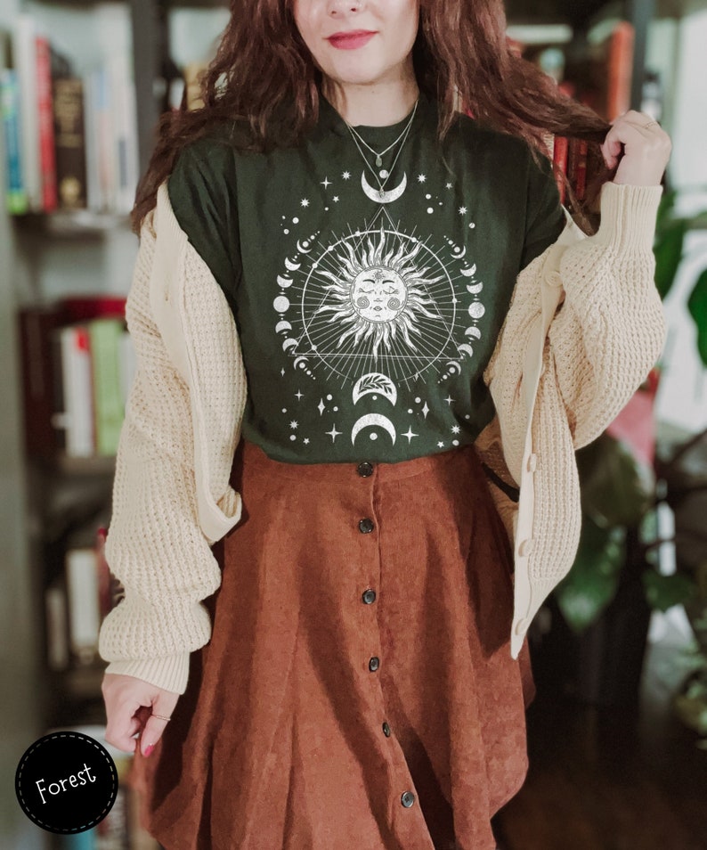 K&ouml;nnte beinhalten: Ein gr&uuml;nes T-Shirt mit einem wei&szlig;en Sonnen- und Monddesign. Das Design zeigt eine Sonne mit einem Gesicht, umgeben von einem Kreis aus Monden und Sternen. Das Shirt wird mit einem braunen Cordrock kombiniert.