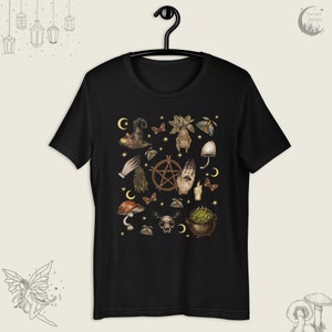 Puede incluir: Camiseta negra con un estampado de varios s&iacute;mbolos y objetos de brujer&iacute;a, incluyendo un pentagrama, un caldero, una mano con un ojo, setas y una luna creciente.