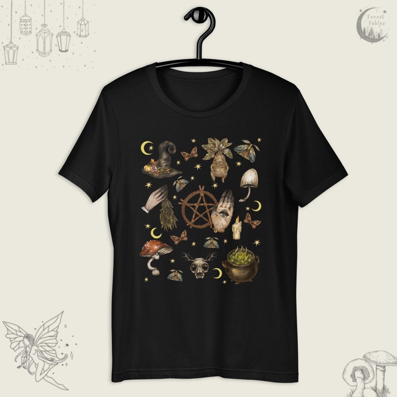 Puede incluir: Camiseta negra con un estampado de varios s&iacute;mbolos y objetos de brujer&iacute;a, incluyendo un pentagrama, un caldero, una mano con un ojo, setas y una luna creciente.
