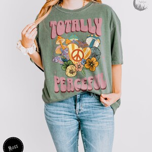 May include: A green t-shirt with a retro-style graphic design featuring the text "Totally Peaceful" in pink letters with a peace sign and flowers.
