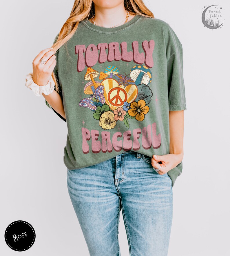 May include: A green t-shirt with a retro-style graphic design featuring the text "Totally Peaceful" in pink letters with a peace sign and flowers.