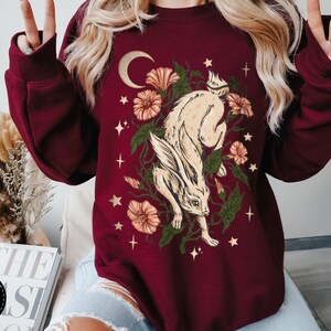 May include: A maroon sweatshirt with a white rabbit jumping through a floral design with stars and a crescent moon.