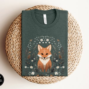 May include: A dark green t-shirt with a graphic of a fox surrounded by white flowers. The fox is orange and white with a black nose and eyes.