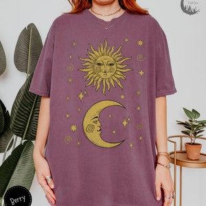 Puede incluir: Una camiseta morada de gran tama&ntilde;o con un gr&aacute;fico vintage de sol y luna. El sol y la luna tienen caras y est&aacute;n rodeados de estrellas. El texto "Forest Fables" est&aacute; en la esquina superior derecha de la imagen.