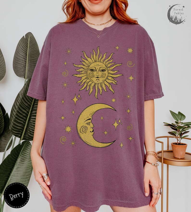Puede incluir: Una camiseta morada de gran tama&ntilde;o con un gr&aacute;fico vintage de sol y luna. El sol y la luna tienen caras y est&aacute;n rodeados de estrellas. El texto "Forest Fables" est&aacute; en la esquina superior derecha de la imagen.