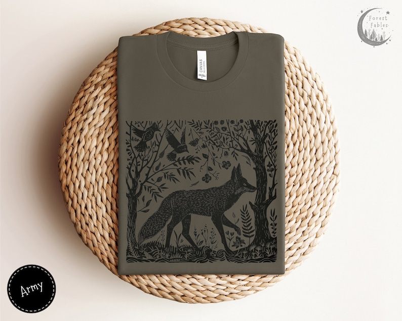 May include: A dark green t-shirt with a black and white illustration of a fox in a forest setting. The illustration includes trees, leaves, and birds. The text "Forest Fables" is in the upper right corner of the image.