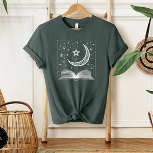 May include: A dark green t-shirt with a white graphic of a crescent moon, stars, and an open book. The graphic is in a square frame.