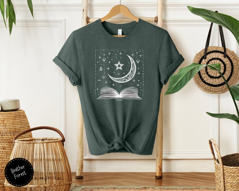 May include: A dark green t-shirt with a white graphic of a crescent moon, stars, and an open book. The graphic is in a square frame.