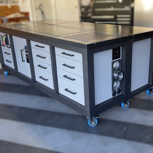 May include: A black and gray workbench with a black top and multiple drawers. The workbench has a built-in power strip and is on wheels.