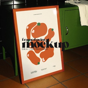 Può includere: Un mockup di stampa incorniciata con una cornice in legno arancione. La stampa presenta forme arancioni astratte con accenti verdi su uno sfondo color crema. Il testo sulla stampa recita "framed print mockup" e "DIN A | FOR PHOTOSHOP".
