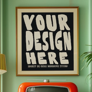 May include: A framed poster with a black background and white text that reads "YOUR DESIGN HERE" with the words "MOCKUP BY EMMA RODRIGUEZ STUDIO" below the text. The poster is hanging on a green wall above a vintage orange television.
